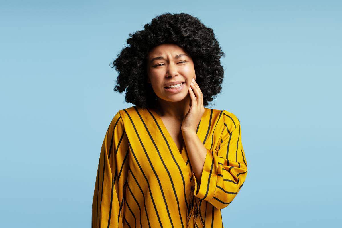 Young woman touching her cheek in pain, showing signs of discomfort.