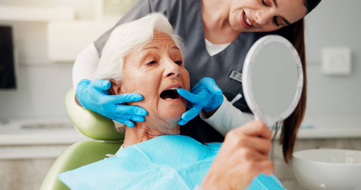 Dentist, senior woman and consulting with mirror for teeth cleaning, dental implant or oral hygiene.